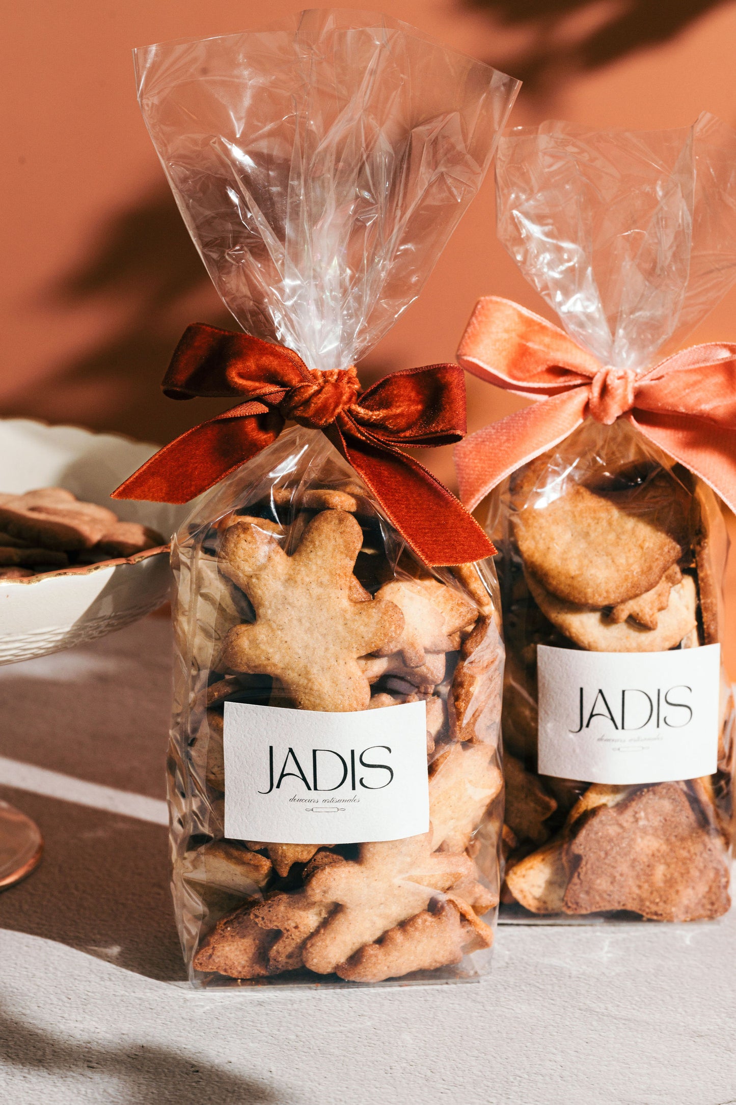 2 sachets de biscuits aux épices et amandes avec des noeuds en velours, sur fond rose.