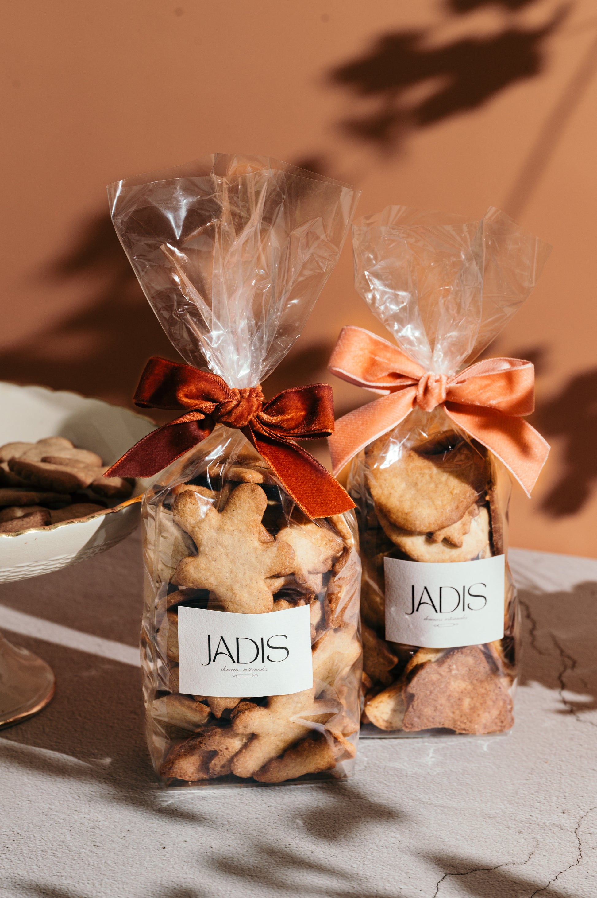 2 sachets de biscuits aux épices et amandes avec des noeuds en velours, sur fond rose.